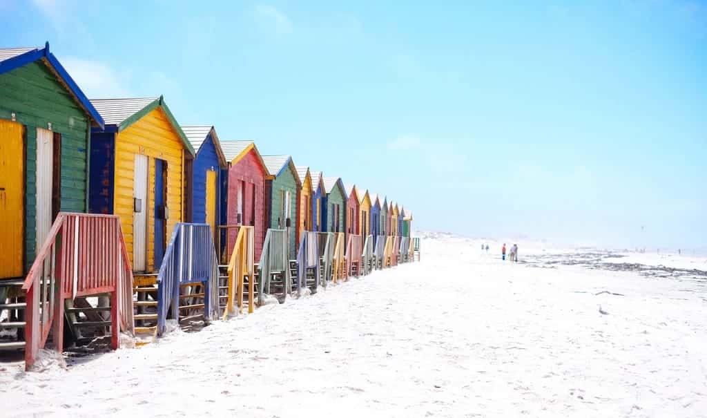 A row of brightly painted beach huts on white sand